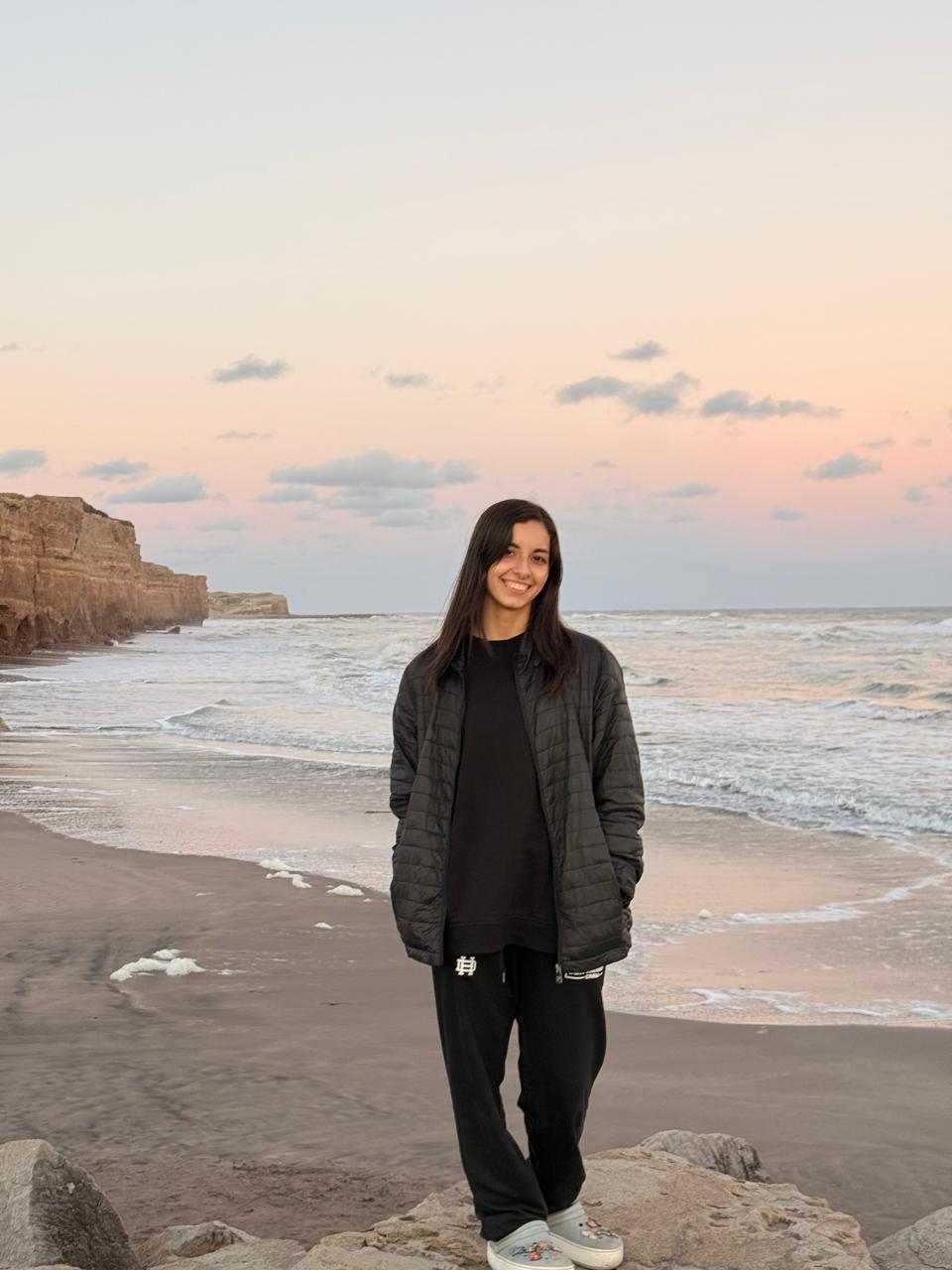 Beska sonriendo, parada en la playa al atardecer.